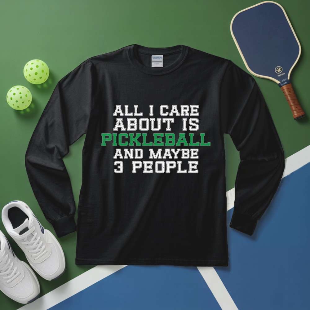 Black long-sleeve shirt with pickleball-themed text on a green and blue surface with pickleball equipment.