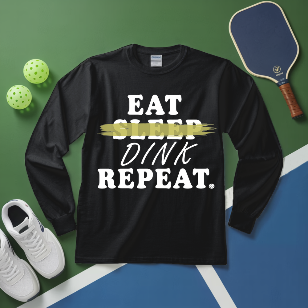 Black long-sleeve shirt with 'Eat Sleep Dink Repeat' text on a sports court background with pickleball equipment.