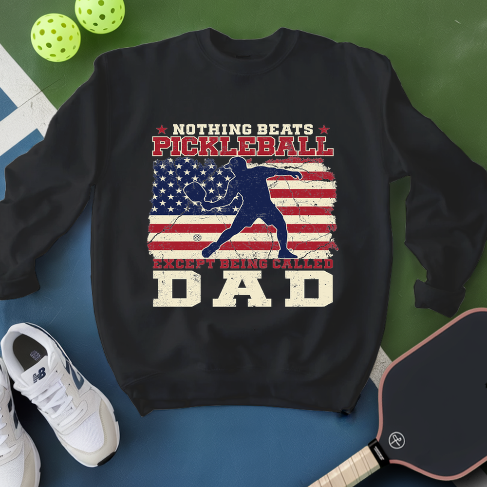Black sweatshirt with pickleball design and text, surrounded by pickleballs and a paddle on a green and blue background.