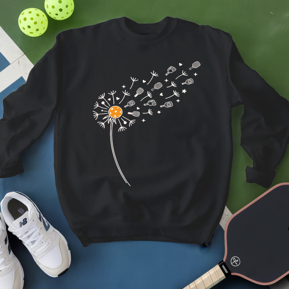 Black sweatshirt with a dandelion graphic on a blue surface with pickleball equipment.