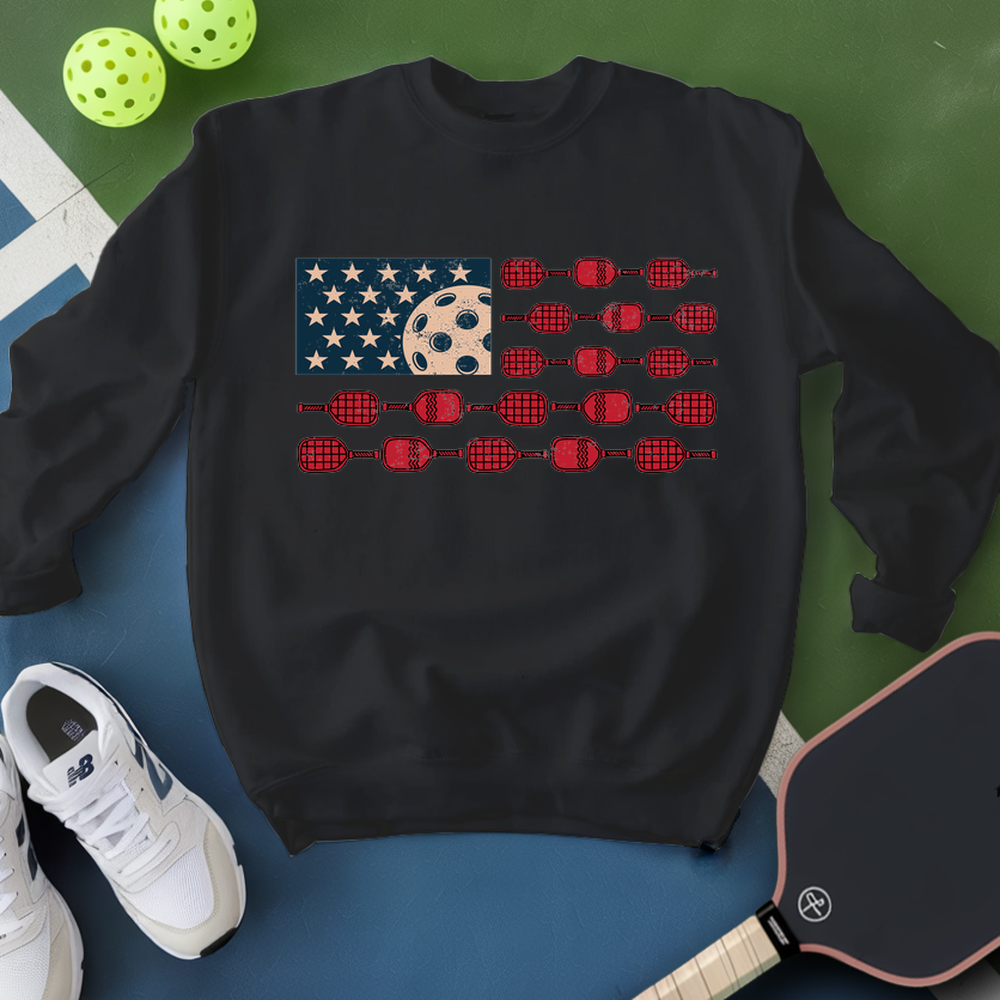 Black sweatshirt with a unique design on a blue surface with pickleball equipment.