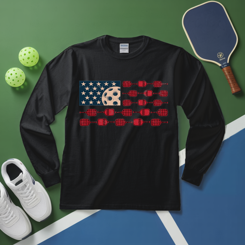 Black long-sleeve shirt with pickleball-themed design on a green and blue surface with pickleball equipment.
