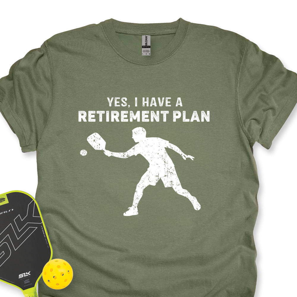 Green t-shirt with 'Yes, I have a retirement plan' text and pickleball player graphic, paired with a pickleball paddle and ball on a white background.