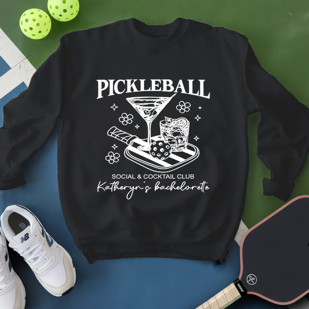 Black sweatshirt with pickleball-themed design on a blue and green background