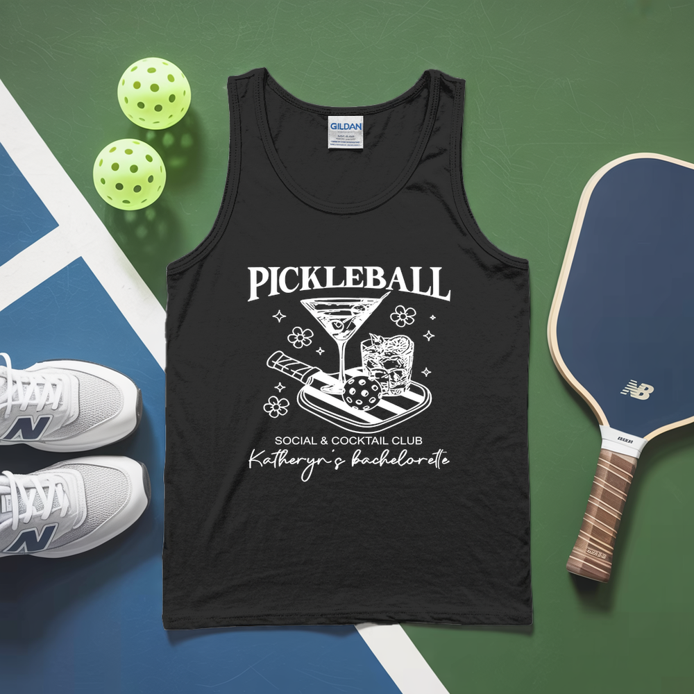 Black tank top with pickleball design on a green and blue surface with pickleballs and paddle.
