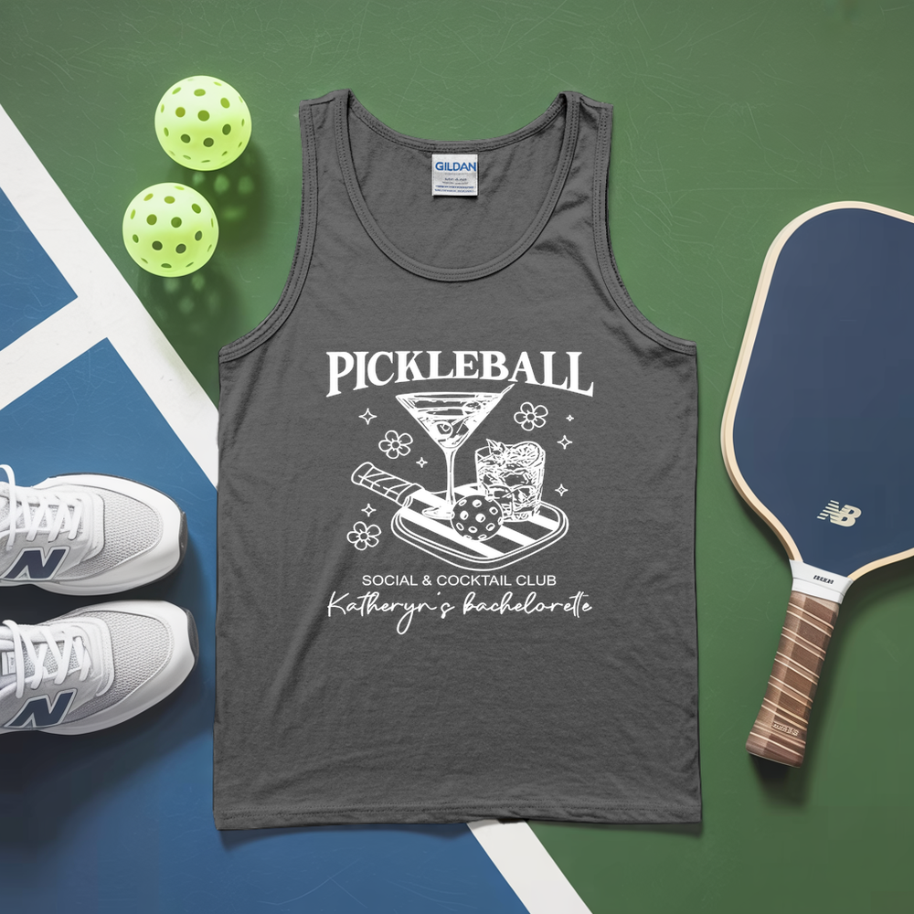 Gray tank top with pickleball-themed design on a green and blue surface with pickleballs and a paddle.