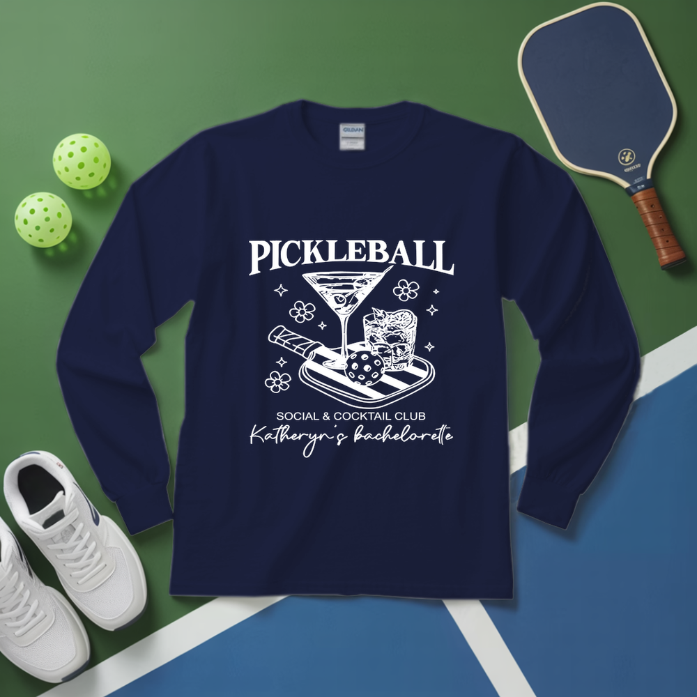 Navy blue sweatshirt with pickleball design on a green and blue surface with pickleballs and a paddle.