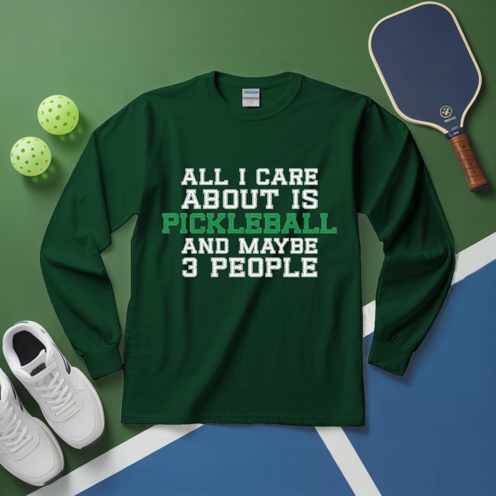 Green long-sleeve shirt with pickleball text on a green and blue surface with pickleball equipment.