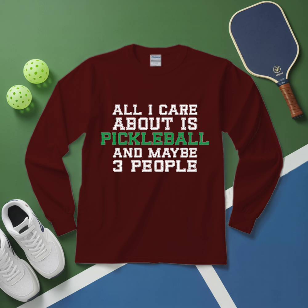 Maroon long-sleeve shirt with pickleball-themed text on a green and blue surface with pickleball equipment.