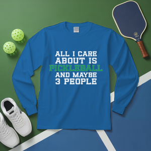 Blue long-sleeve shirt with pickleball-themed text on a green and blue surface with pickleball equipment.
