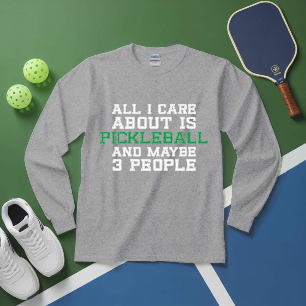 Gray long-sleeve shirt with pickleball-themed text on a green and blue surface with pickleball equipment.
