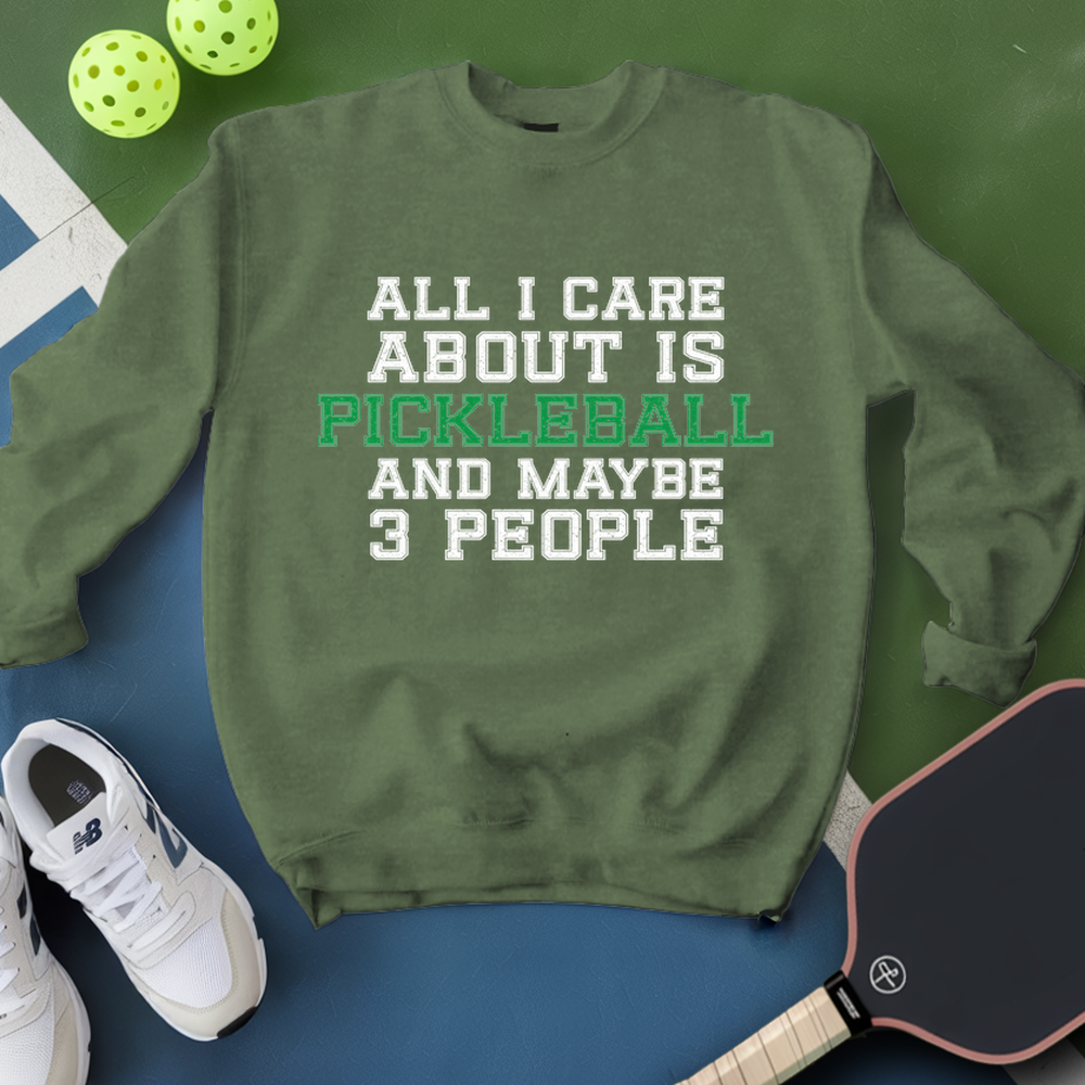 Green sweatshirt with text 'All I care about is pickleball and maybe 3 people' on a blue and green background with pickleball equipment.