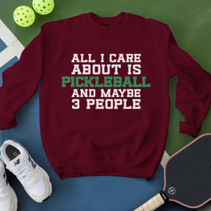 Maroon sweatshirt with pickleball text, pickleballs, and paddle on a green and blue background