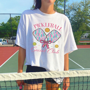 Person wearing a white t-shirt with pickleball-themed design on a tennis court
