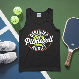 Black tank top with 'Certified Pickleball Addict' text, pickleballs, and paddle on a green and blue surface.