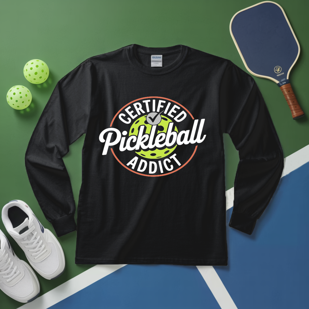 Black long-sleeve shirt with 'Certified Pickleball Addict' design on a green and blue surface with pickleball equipment.