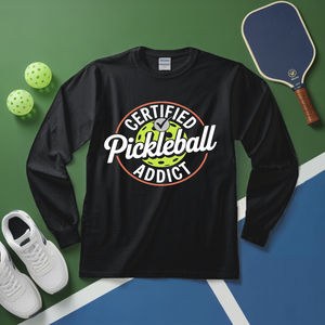 Black long-sleeve shirt with 'Certified Pickleball Addict' design on a green and blue surface with pickleball equipment.
