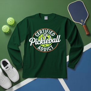 Green long-sleeve shirt with 'Certified Pickleball Addict' design on a green and blue surface with pickleball equipment.