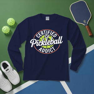 Navy blue sweatshirt with 'Certified Pickleball Addict' design on a green and blue surface with pickleball equipment.