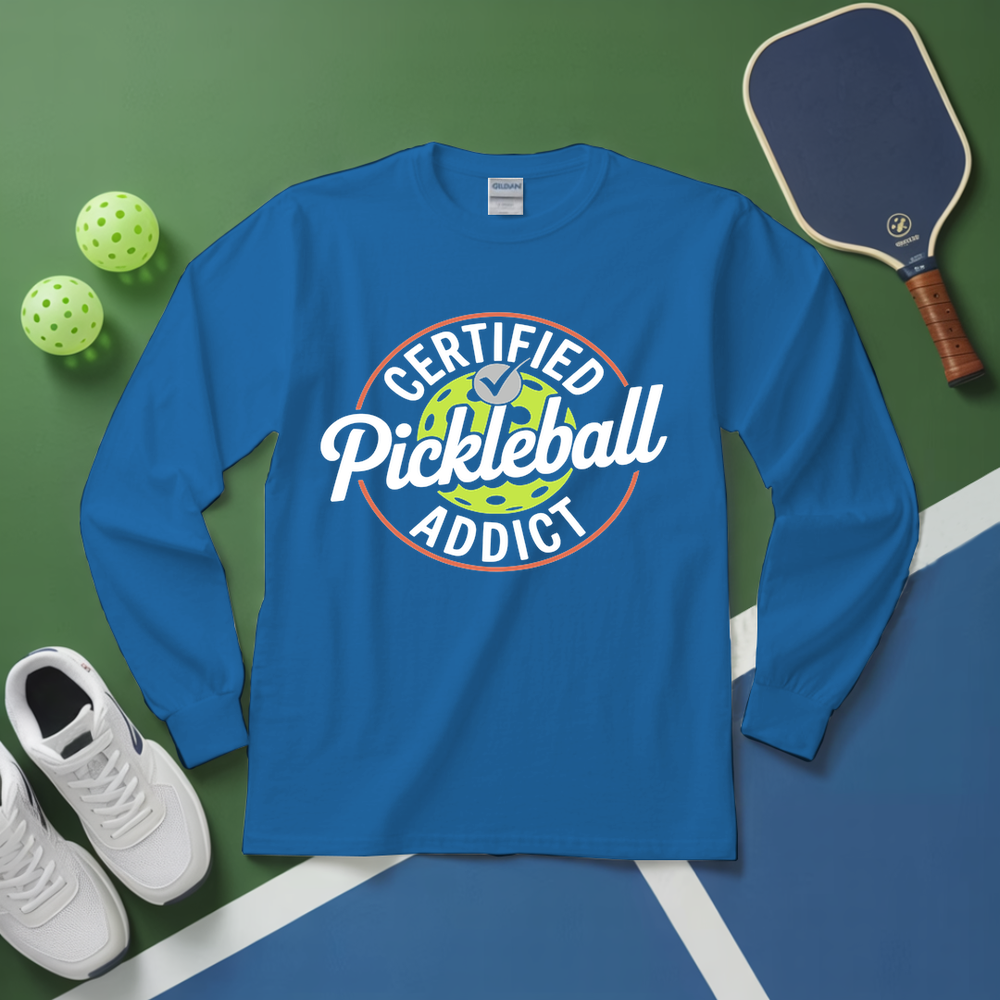 Blue long-sleeve shirt with 'Certified Pickleball Addict' design on a green and blue surface with pickleball equipment.