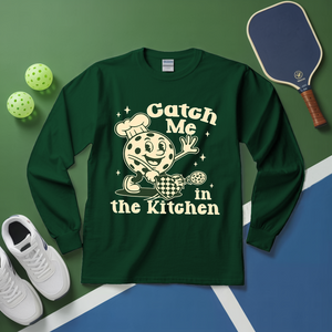 Green long-sleeve shirt with a pizza graphic and text on a green and blue surface with sports equipment.