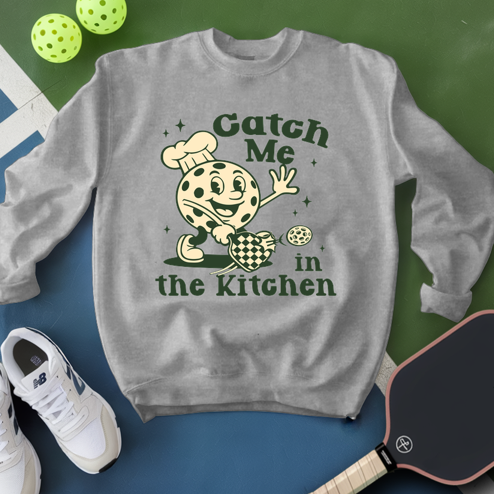 Gray sweatshirt with a cartoon character and text 'Catch Me in the Kitchen' on a green and blue background.