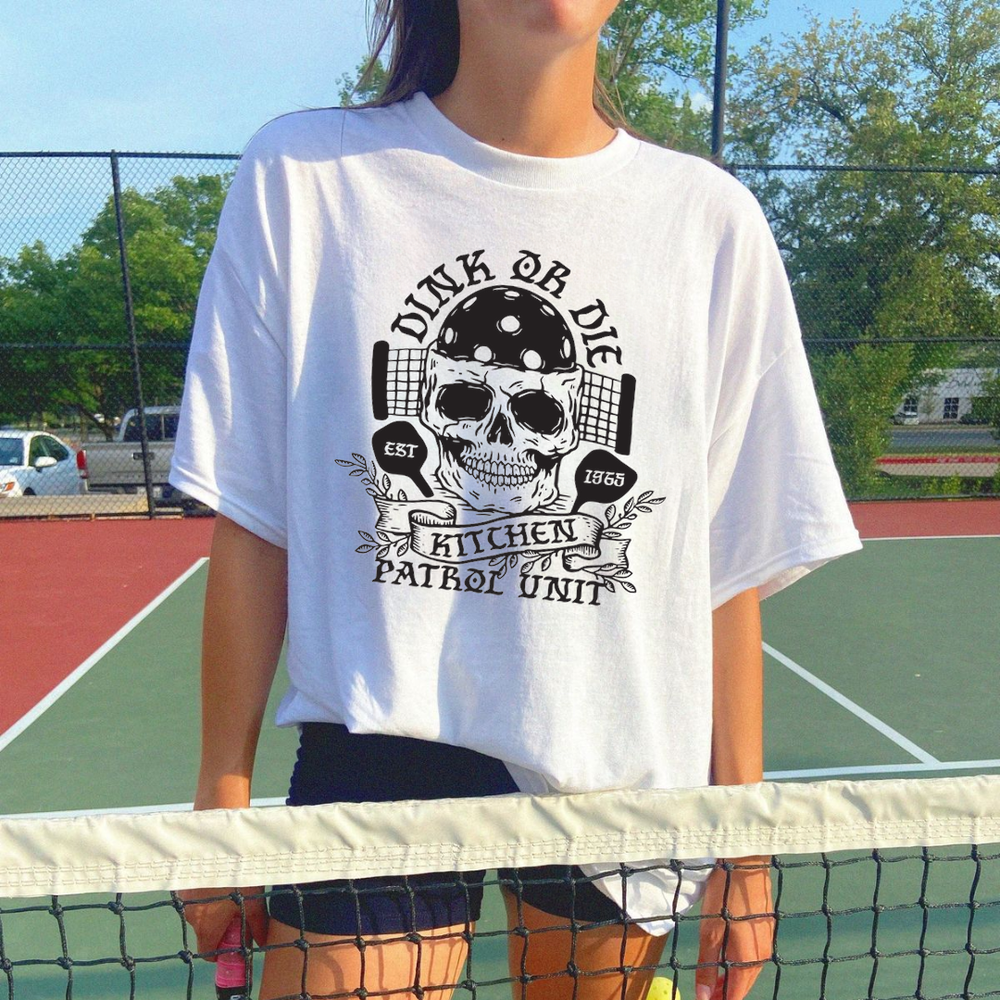 Person wearing a white t-shirt with a graphic design on a tennis court