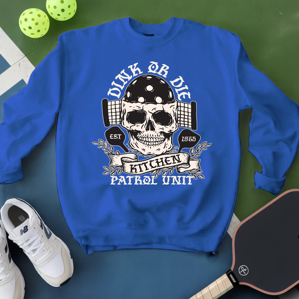 Blue sweatshirt with skull design and text on a green surface with pickleball equipment.