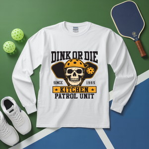White long-sleeve shirt with skull graphic and text on a green and blue background with pickleball equipment.