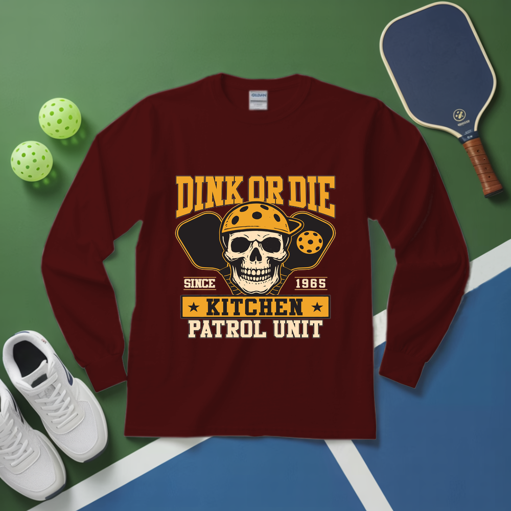 Maroon long-sleeve shirt with skull design and text on a green and blue surface with pickleball equipment.