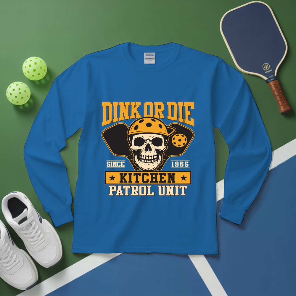 Blue long-sleeve shirt with skull graphic and text on a green and blue surface with pickleball equipment.