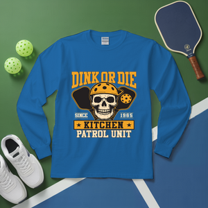Blue long-sleeve shirt with skull graphic and text on a green and blue surface with pickleball equipment.