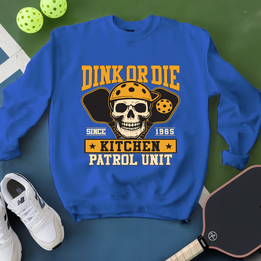 Blue sweatshirt with skull graphic and text on a green surface with pickleball equipment.
