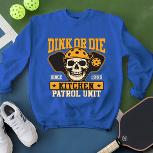 Blue sweatshirt with skull graphic and text on a green surface with pickleball equipment.