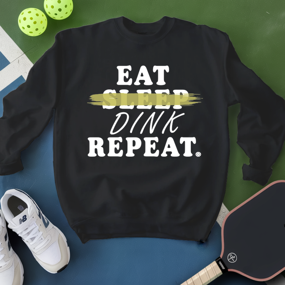 Black sweatshirt with 'Eat Sleep Dink Repeat' text, white sneakers, and pickleball equipment on a green and blue background.
