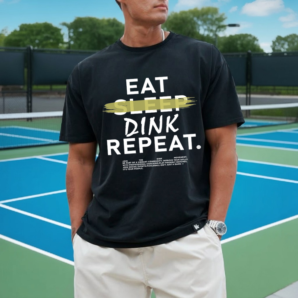 Person wearing a black t-shirt with 'EAT SLEEP DINK REPEAT' text on a tennis court.