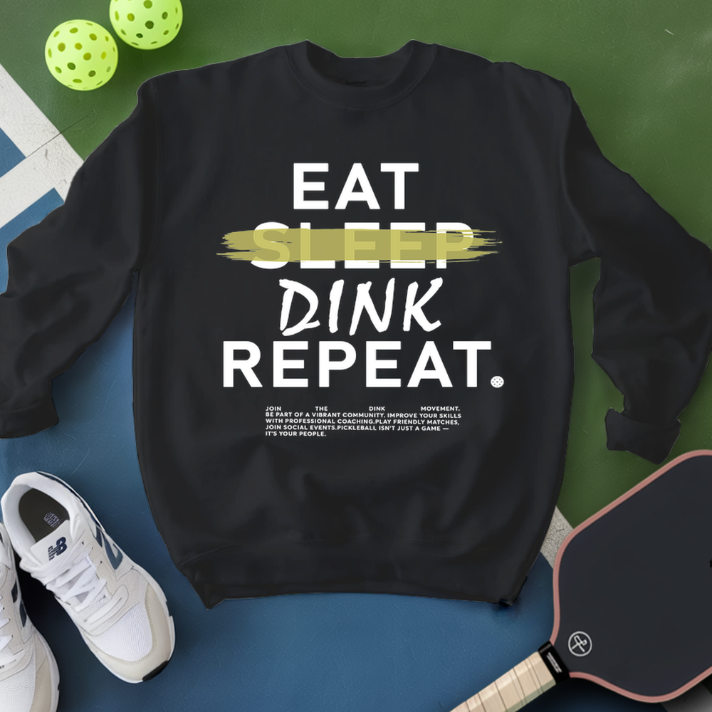 Black sweatshirt with 'EAT SLEEP DINK REPEAT' text, surrounded by pickleball equipment on a green and blue background.