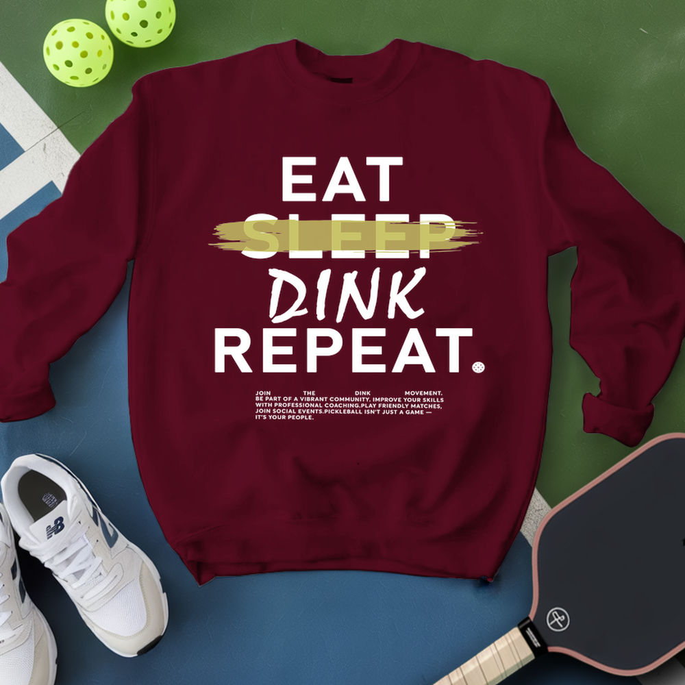 Maroon sweatshirt with 'Eat Sleep Dink Repeat' text, pickleball balls, and paddle on a green and blue background