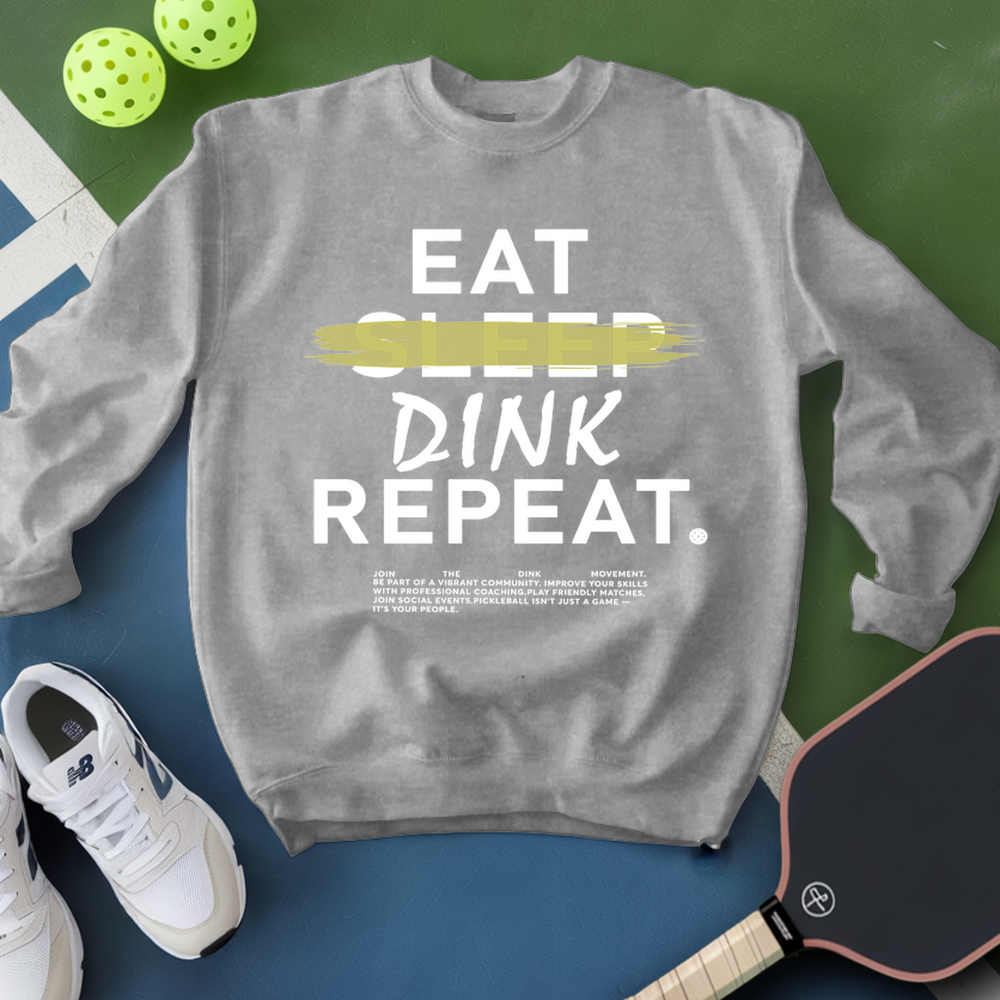 Gray sweatshirt with 'EAT SLEEP DINK REPEAT' text, pickleball balls, paddle, and shoes on a green and blue background