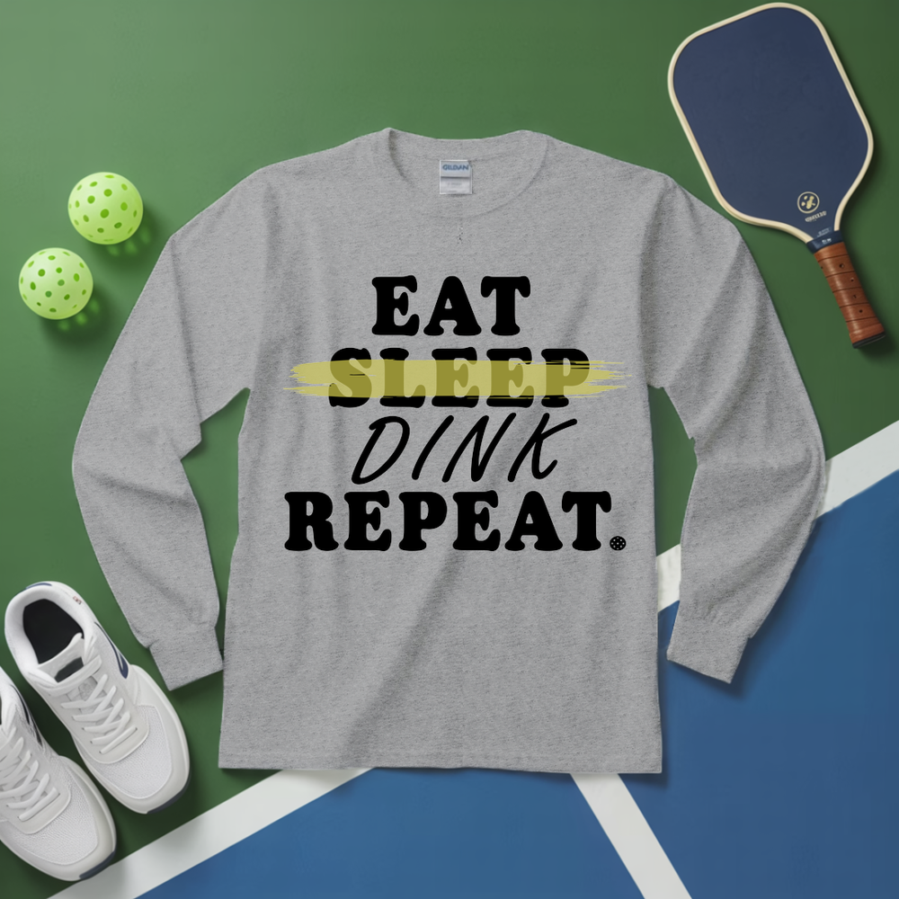 Gray long-sleeve shirt with 'Eat Sleep Dink Repeat' text on a sports-themed background with pickleball equipment.