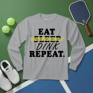 Gray long-sleeve shirt with 'Eat Sleep Dink Repeat' text on a sports-themed background with pickleball equipment.