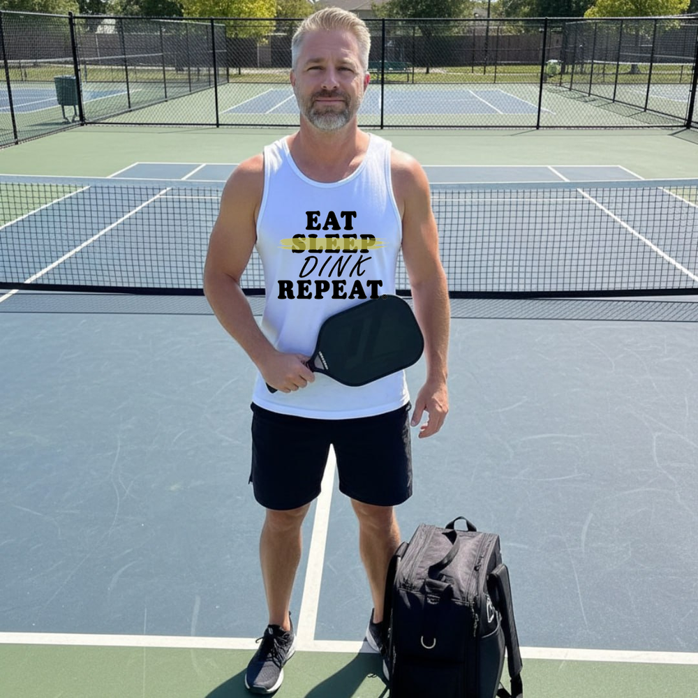 Man on a pickleball court wearing a tank top with text, holding a paddle and bag.