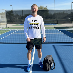 Man on a tennis court wearing a shirt with motivational text, holding a paddle.