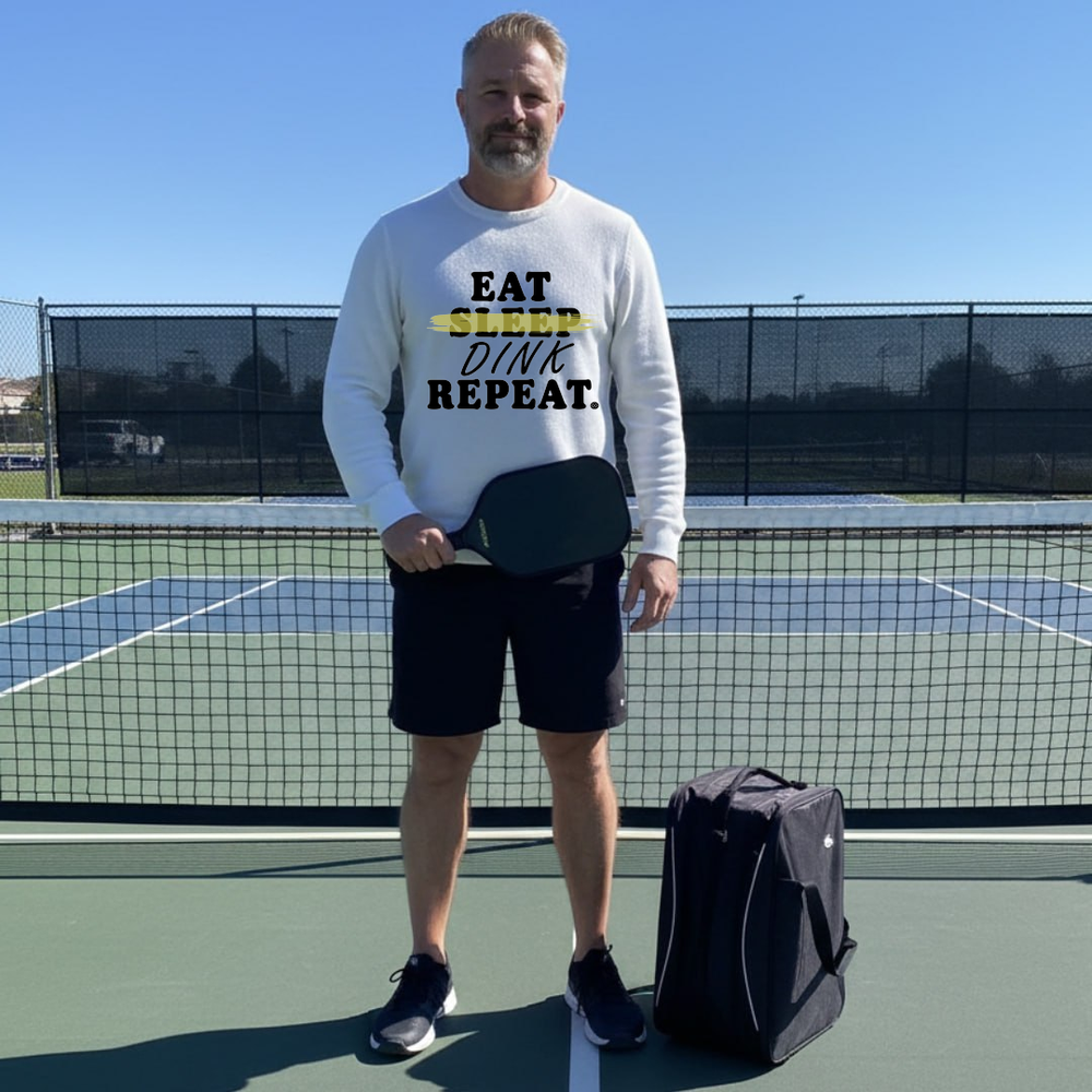 Man on a tennis court holding a paddle with text, standing next to a bag.