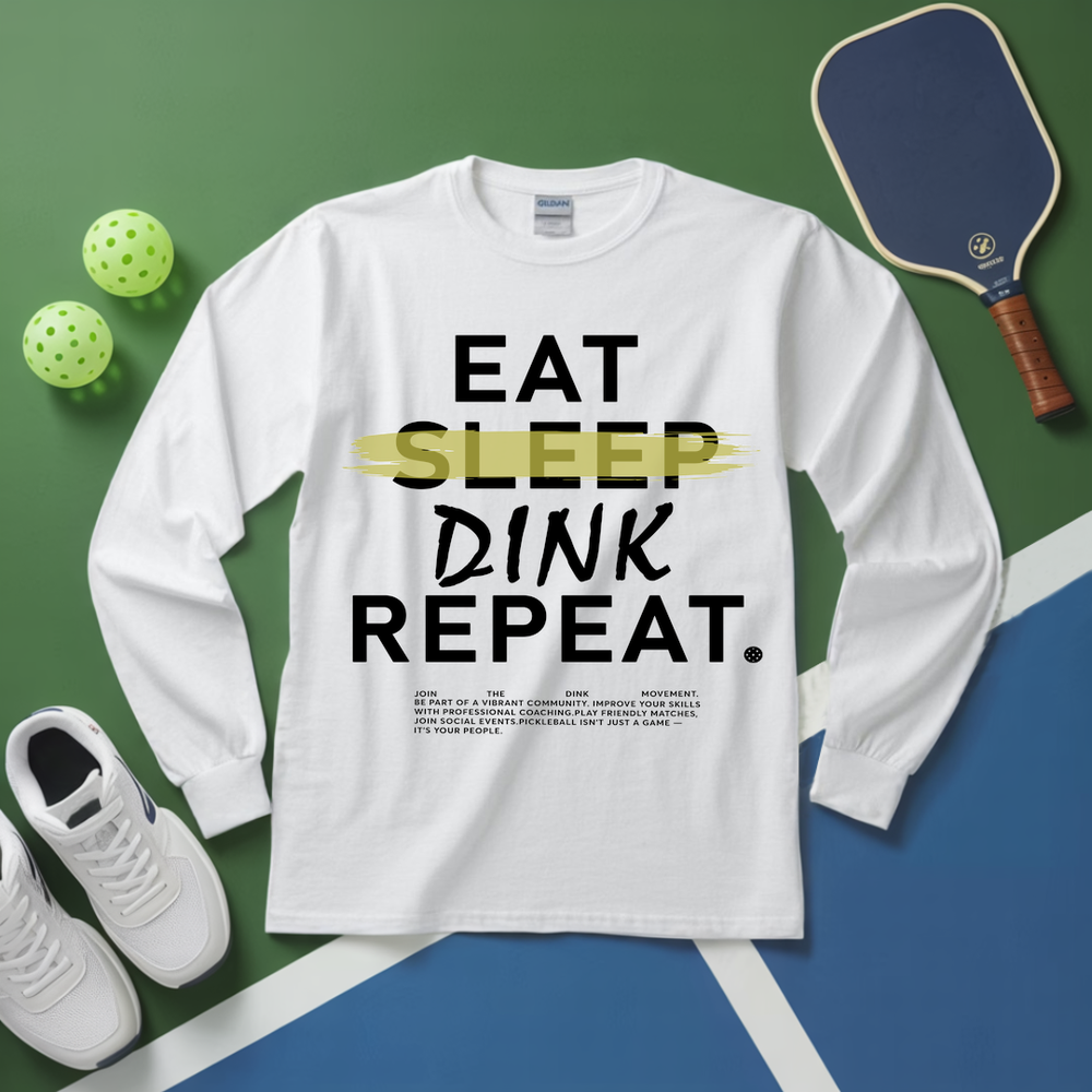 White long-sleeve shirt with 'EAT SLEEP DINK REPEAT' text on a sports-themed background with pickleball equipment.