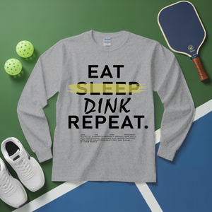 Gray long-sleeve shirt with 'EAT SLEEP DINK REPEAT' text, pickleball equipment on a green and blue background