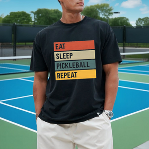 Person wearing a black t-shirt with 'Eat Sleep Pickleball Repeat' text on a pickleball court.