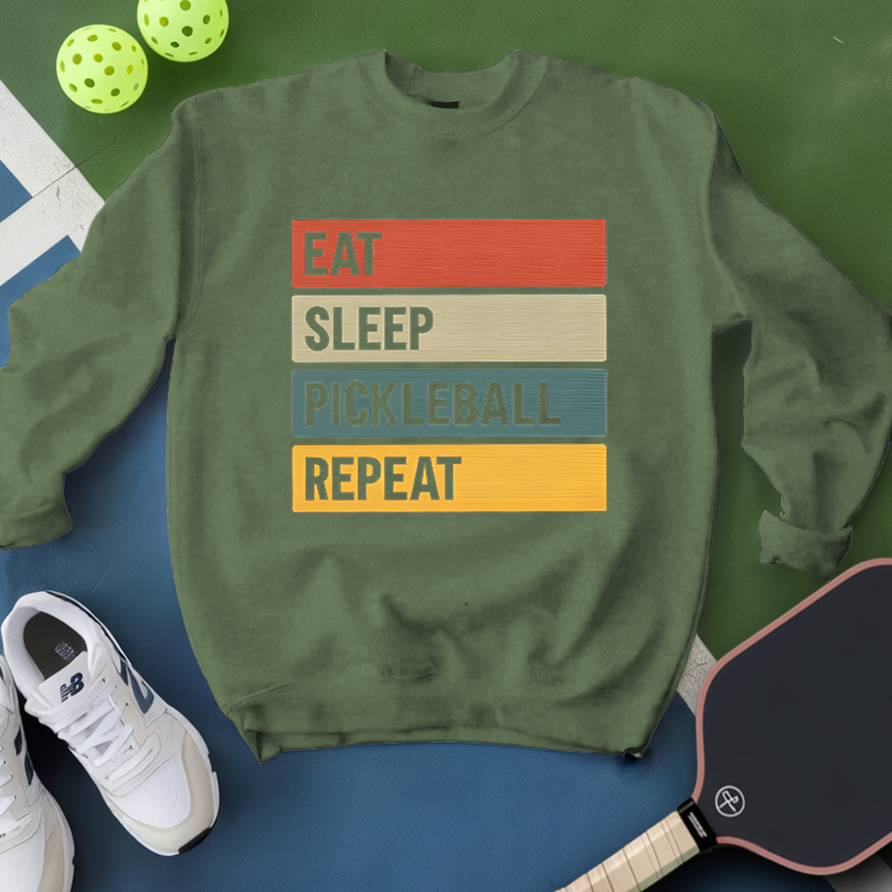 Green sweatshirt with 'Eat Sleep Pickleball Repeat' text, pickleball paddle, and balls on a green and blue background