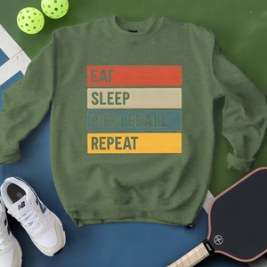 Green sweatshirt with 'Eat Sleep Pickleball Repeat' text, pickleball paddle, and balls on a green and blue background