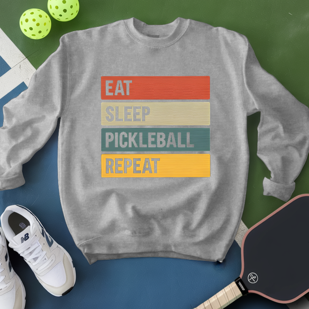 Gray sweatshirt with 'Eat Sleep Pickleball Repeat' text, pickleball paddles, and balls on a green and blue background